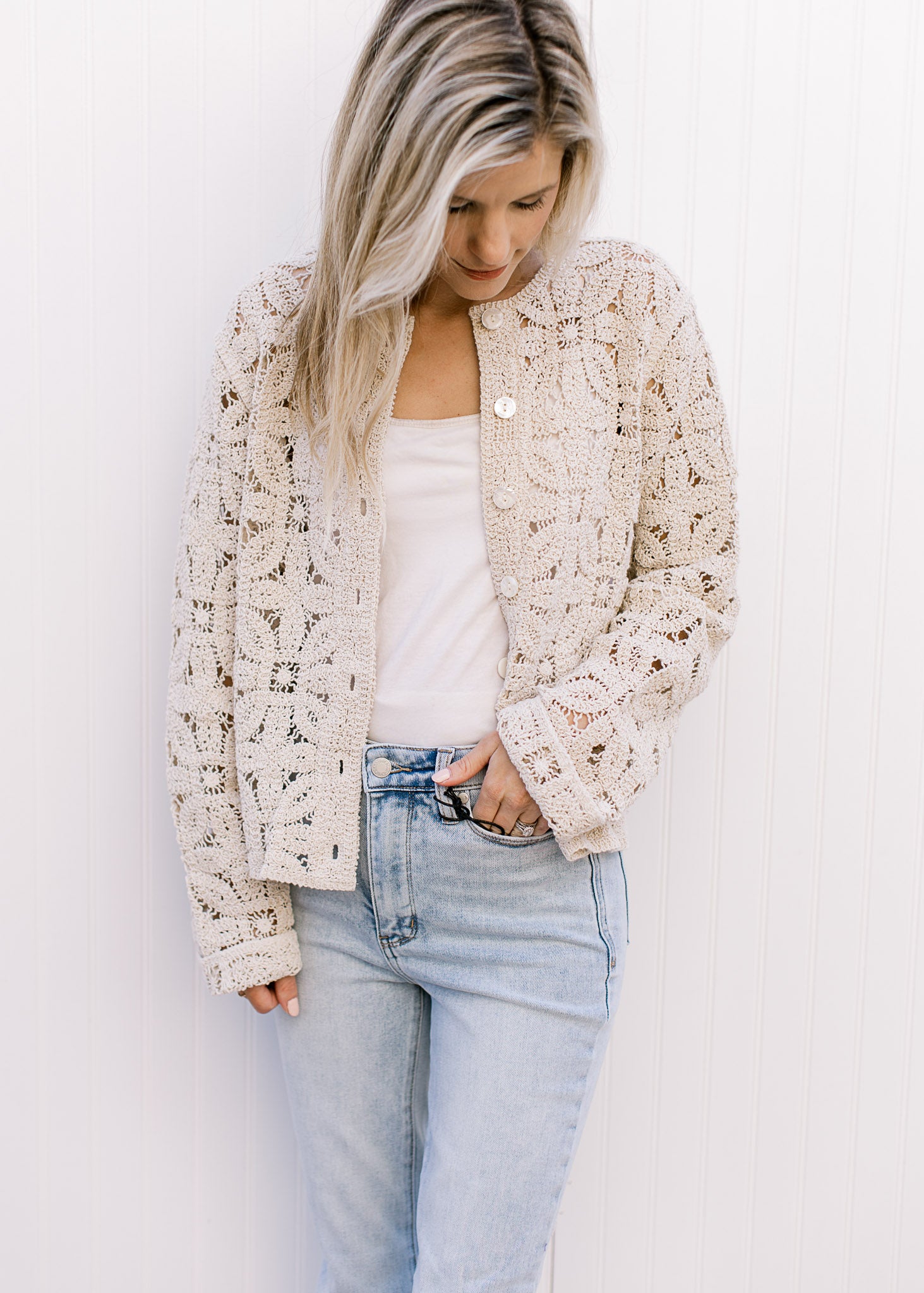 Model wearing jeans and a taupe floral crochet cardigan with a button front and long sleeves. 