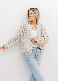Model wearing a taupe button up cardigan with floral crochet, long sleeves and buttons. 