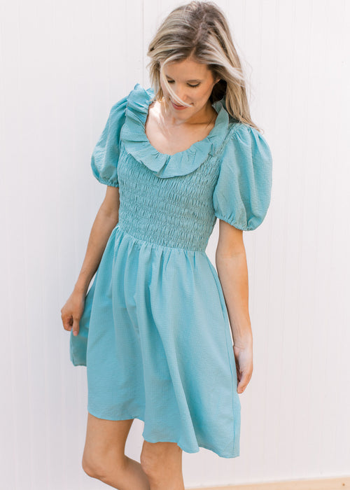 Model wearing a soft teal dress with a smocked bodice, ruffle scooped beck and short puff sleeves.