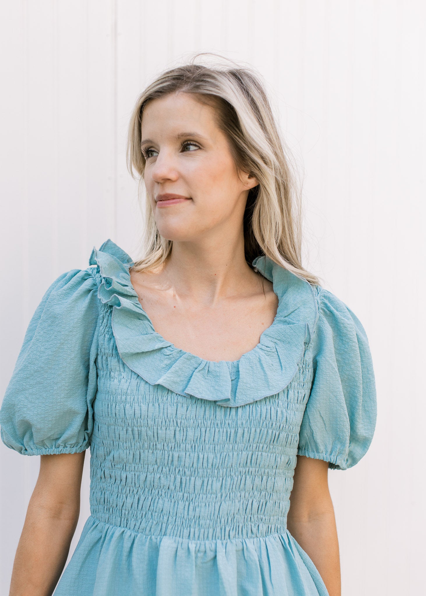 Close up of smocked bodice and ruffle scoop neck on a soft teal above the knee dress.