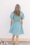 Back view of a soft teal dress with a smocked bodice, ruffle scoop neck and short puff sleeves.