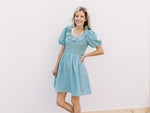 Model wearing a soft teal above the knee dress with a smocked bodice and ruffle scoop neck.
