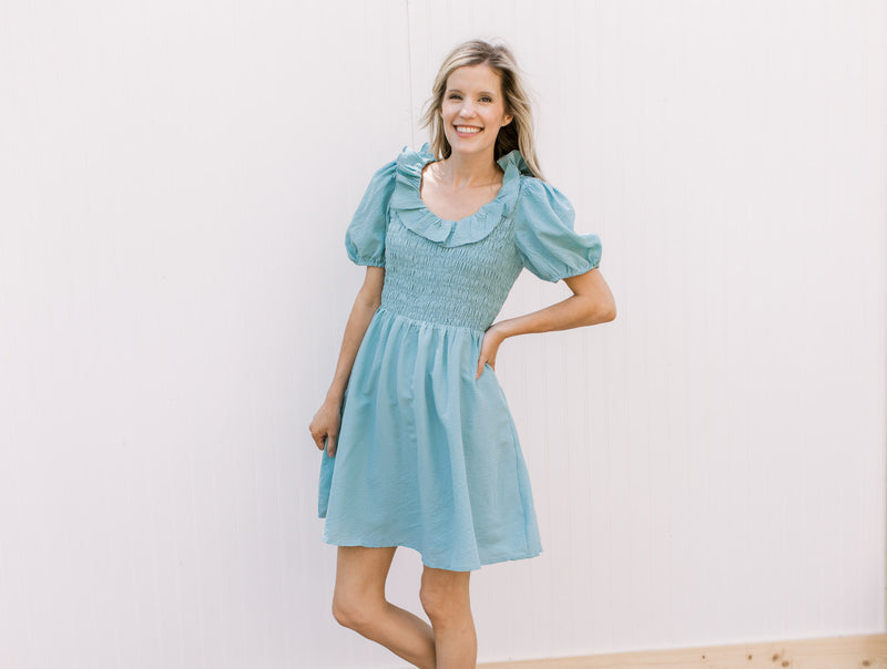 Model wearing a soft teal above the knee dress with a smocked bodice and ruffle scoop neck.