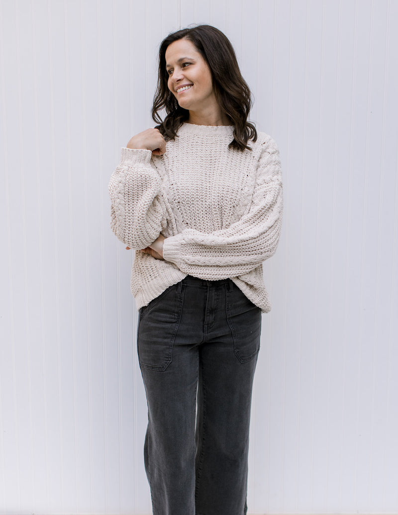 Model wearing jeans and an ivory cable knit sweater with long sleeves and a polyester material.
