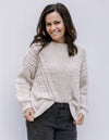 Model wearing an ivory cable knit sweater with long sleeves, crew neck and a polyester material. 