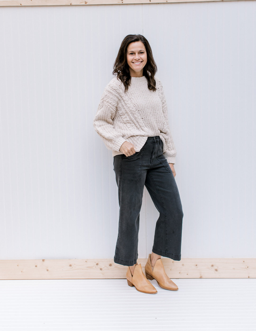 Model wearing jeans, booties and an ivory cable knit sweater with long sleeves and a crew neck. 
