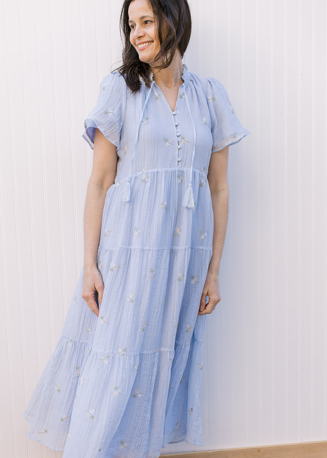 Model wearing a pale blue midi with embroidered floral, v-neck with tie and button placket.