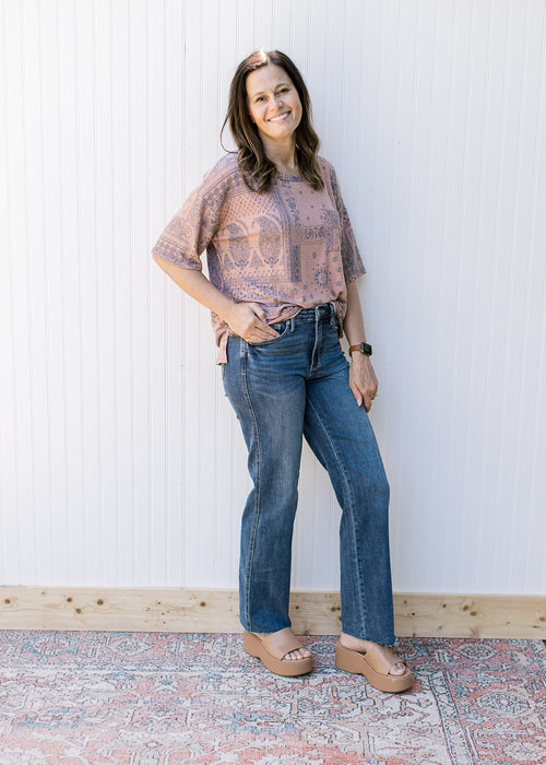 Model wearing jeans, wedges and a light brown top with a navy southwestern pattern.