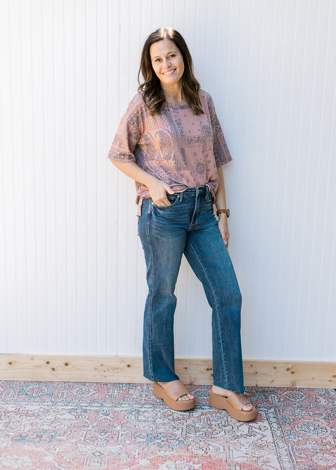Model wearing jeans and a light brown top with a navy southwestern print and a round neck.