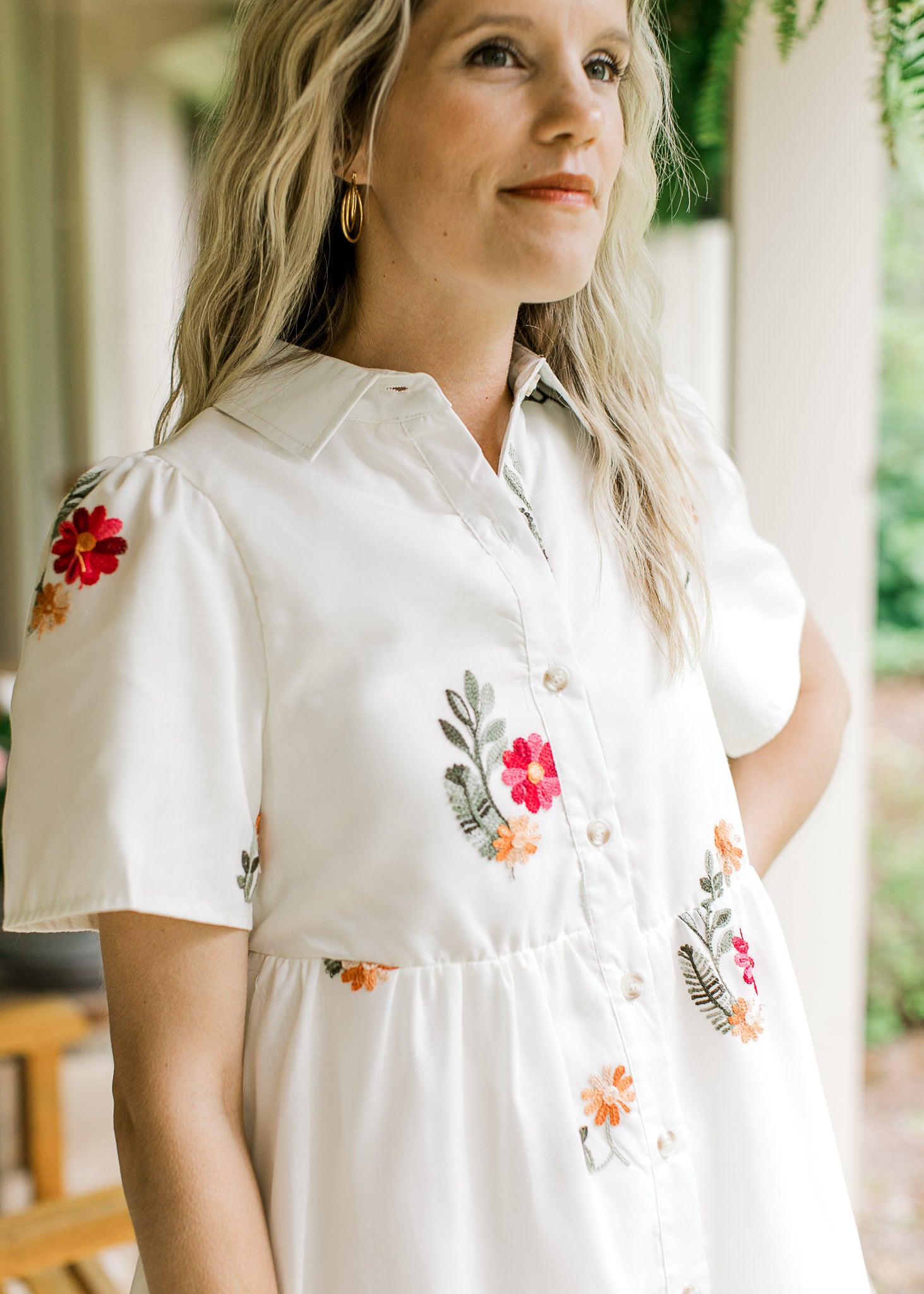 Model wearing a white dress with red, orange and green embroidered floral and short sleeves.