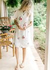 Model wearing a short sleeve button up dress with bright embroidered flowers and a collar.