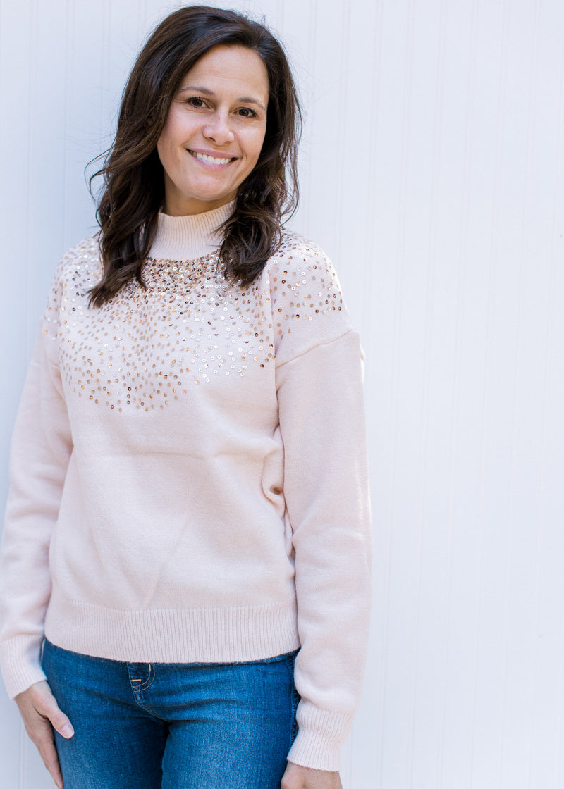 Model wearing a blush colored sweater with sequins at the mock neck and long sleeves. 