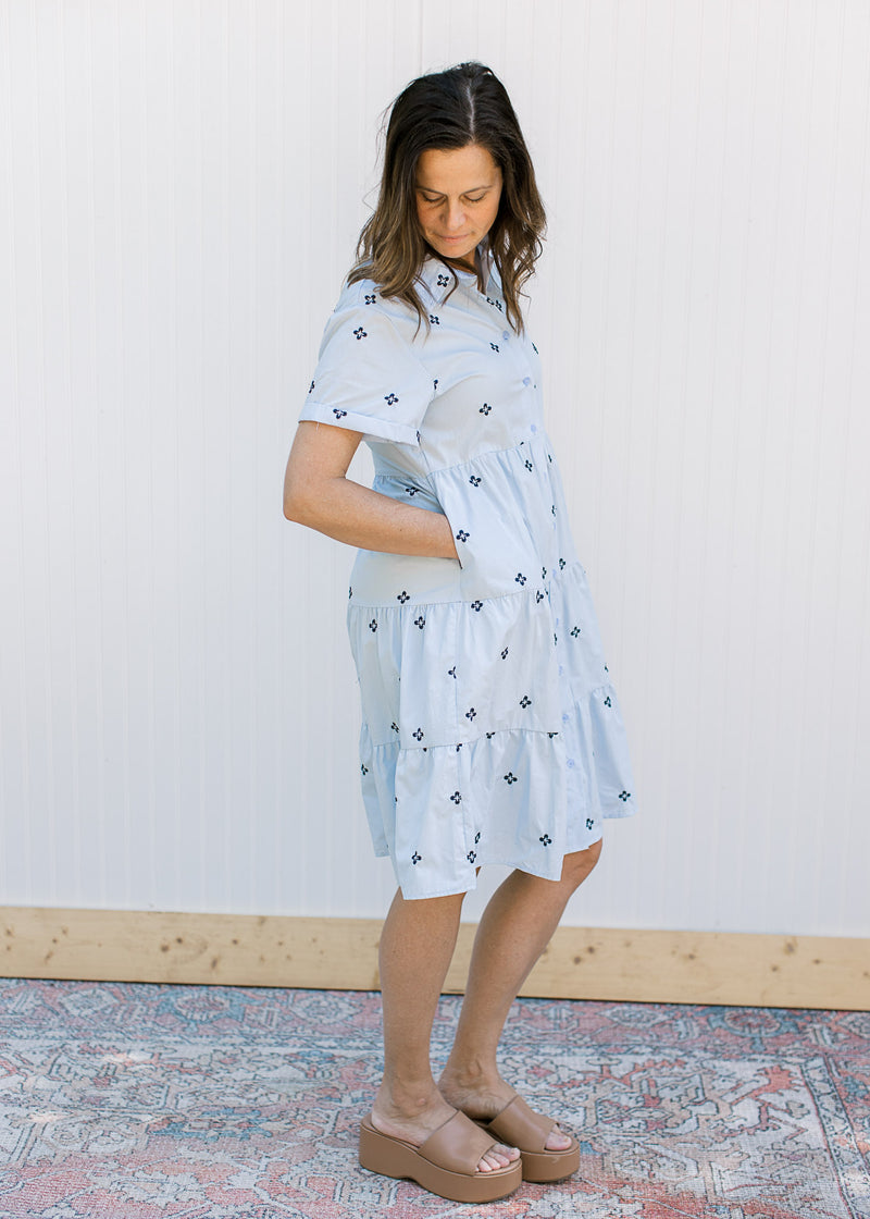 Model wearing a light blue dress with navy embroidered flowers, pockets and short sleeves.