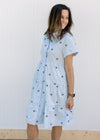 Model wearing a light blue dress with navy embroidered flowers, tiers and short sleeves.