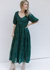 Model wearing a teal midi with short bubble sleeves and a textured leaf overlay and a v-neck. 