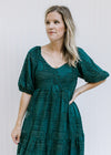 Model wearing a teal midi with a tiered design, short bubble sleeves and a textured leaf overlay. 