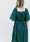 Back view of Model wearing a teal midi with a square back, short sleeves and a leaf overlay. 