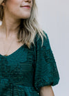 Close up of bubble short sleeves and v-neck on a teal midi with a textured leaf overlay. 