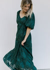 Model wearing a flowy teal midi with short bubble sleeves, v-neck and a textured leaf overlay. 