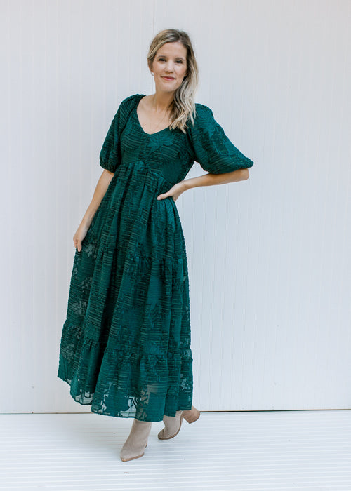 Model wearing a teal, fully lined midi with short bubble sleeves and a textured leaf overlay. 