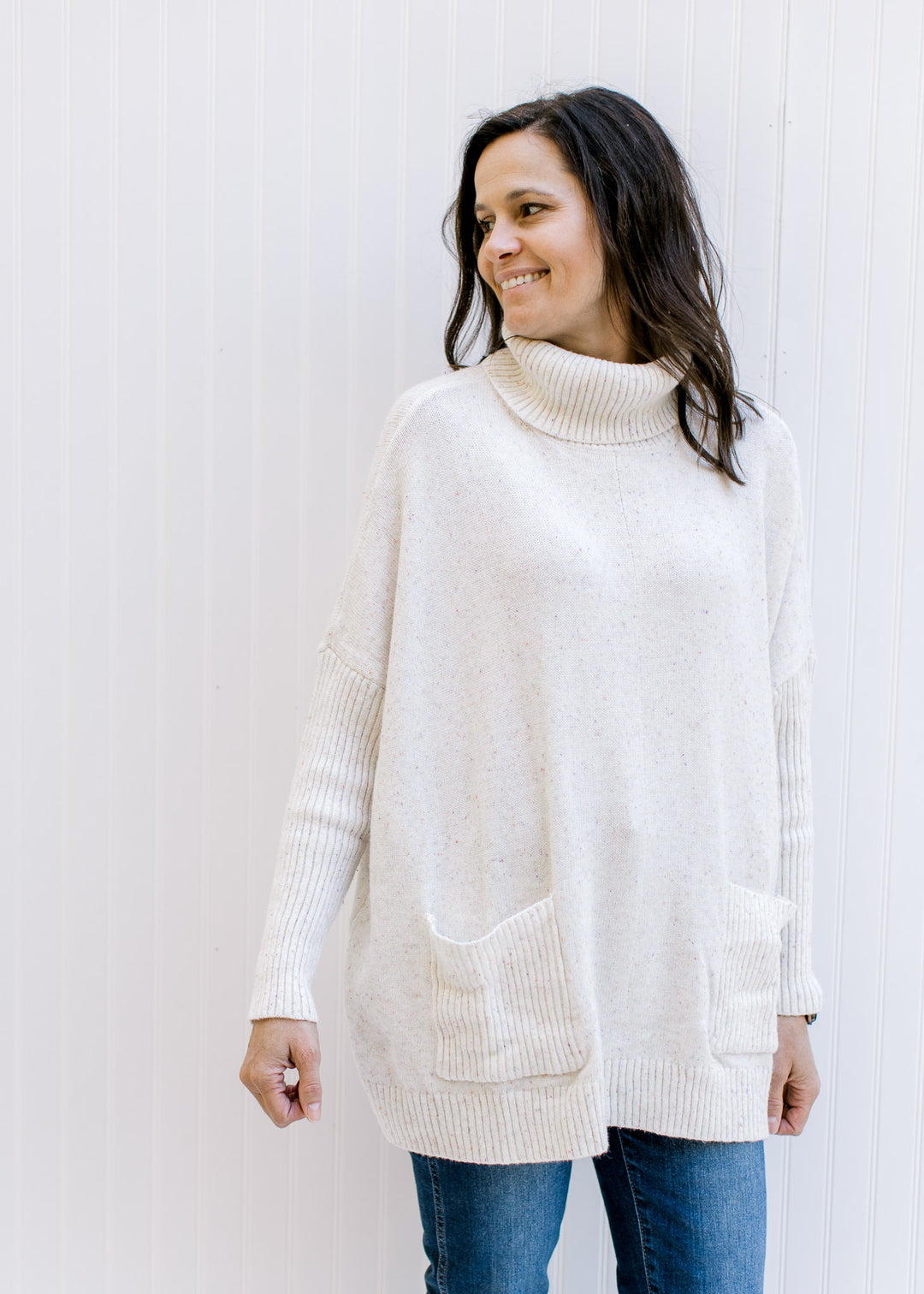 Model wearing jeans with a speckled cream knit sweater with a turtleneck and long sleeves. 