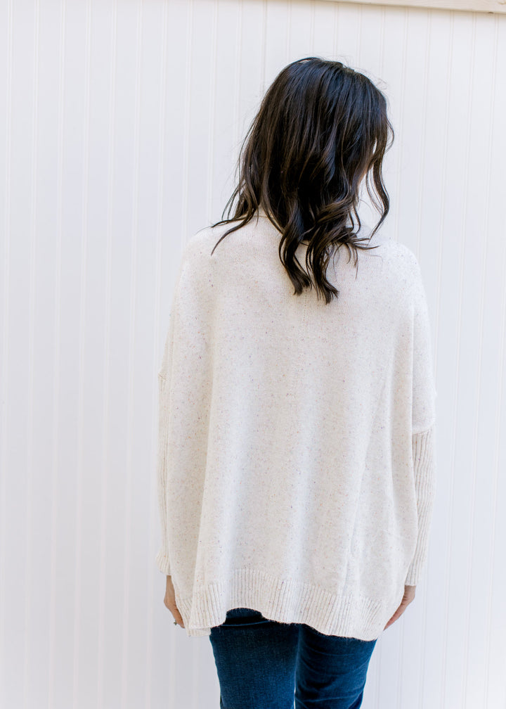 Back view of Model wearing a speckled cream knit sweater with a turtleneck and long sleeves. 