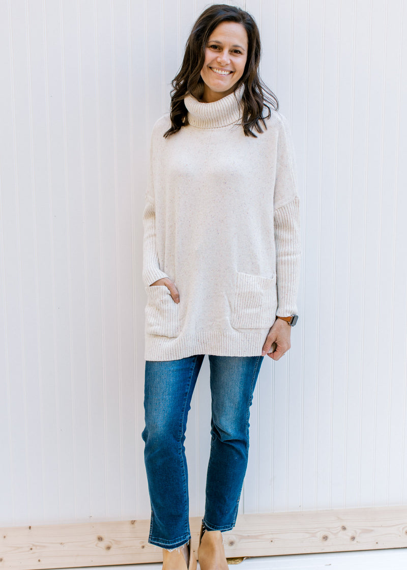 Model wearing jeans and mules with a speckled cream knit sweater with a turtleneck and long sleeves.