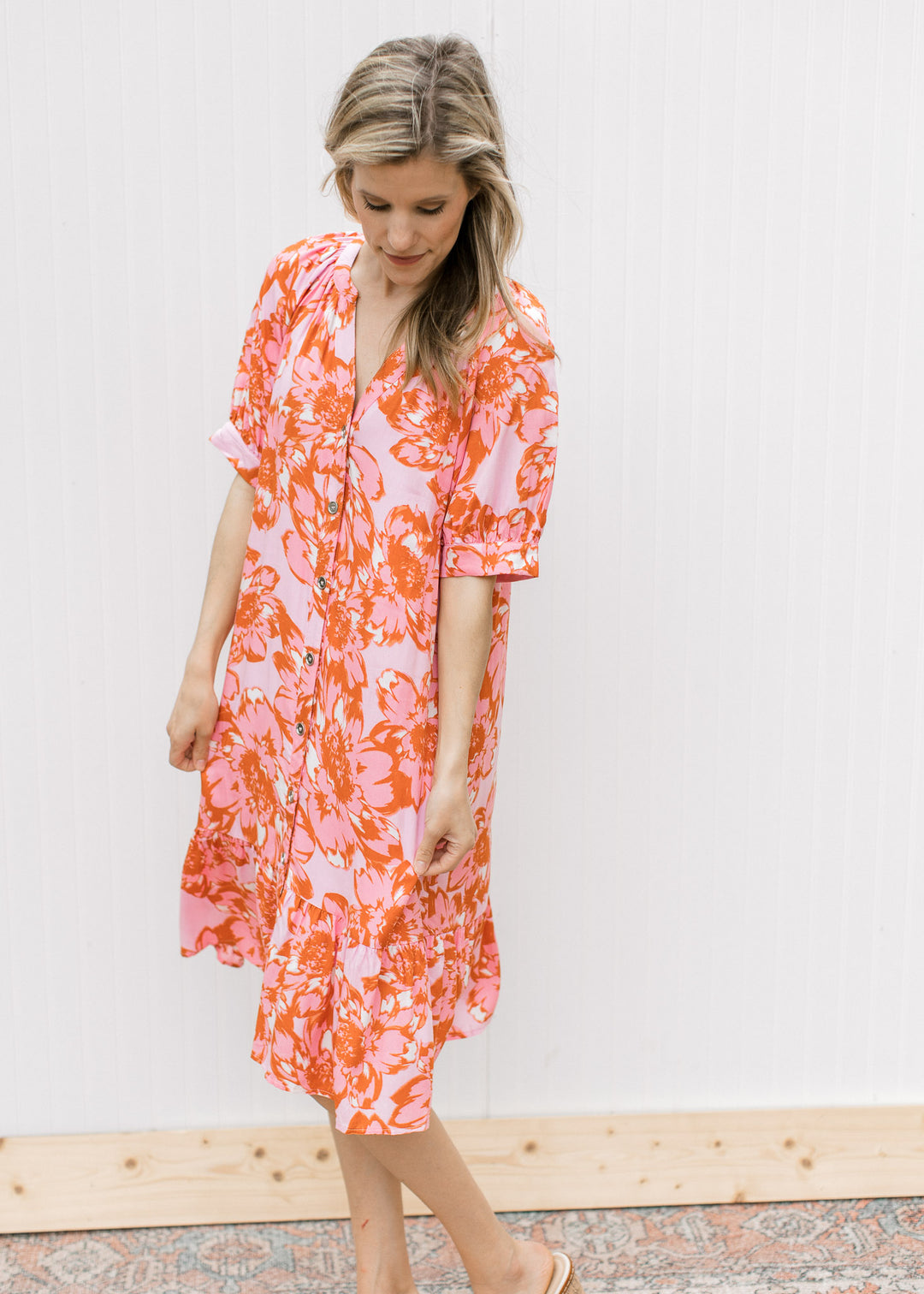 Model wearing a light pink v-neck dress with pink and orange floral, button front and short sleeves.