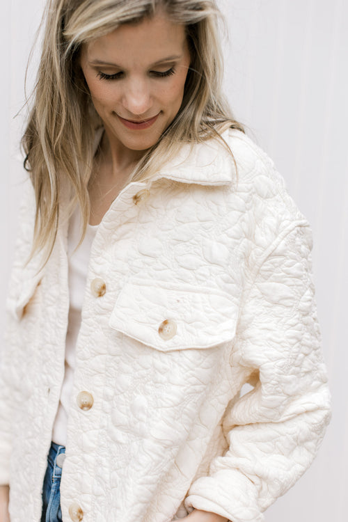 Model wearing a cream embossed shacket with button closure, long sleeves and patch pockets. 