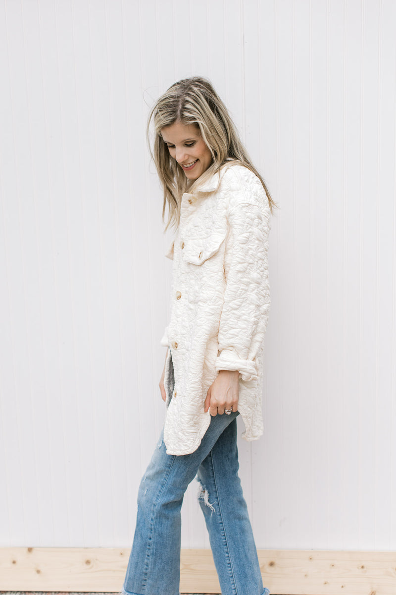 Model wearing a cream embossed shacket with button closure with rolled long sleeves.