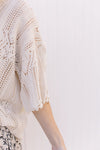 Close up of open weave and scalloping on the sleeve of a cream short sleeve sweater. 