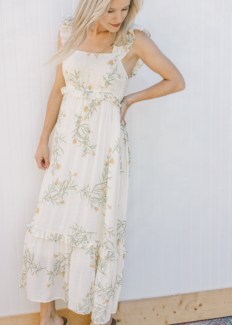 Model wearing a sleeveless, yellowy cream midi with floral, ruffle tiers and a square neck. 