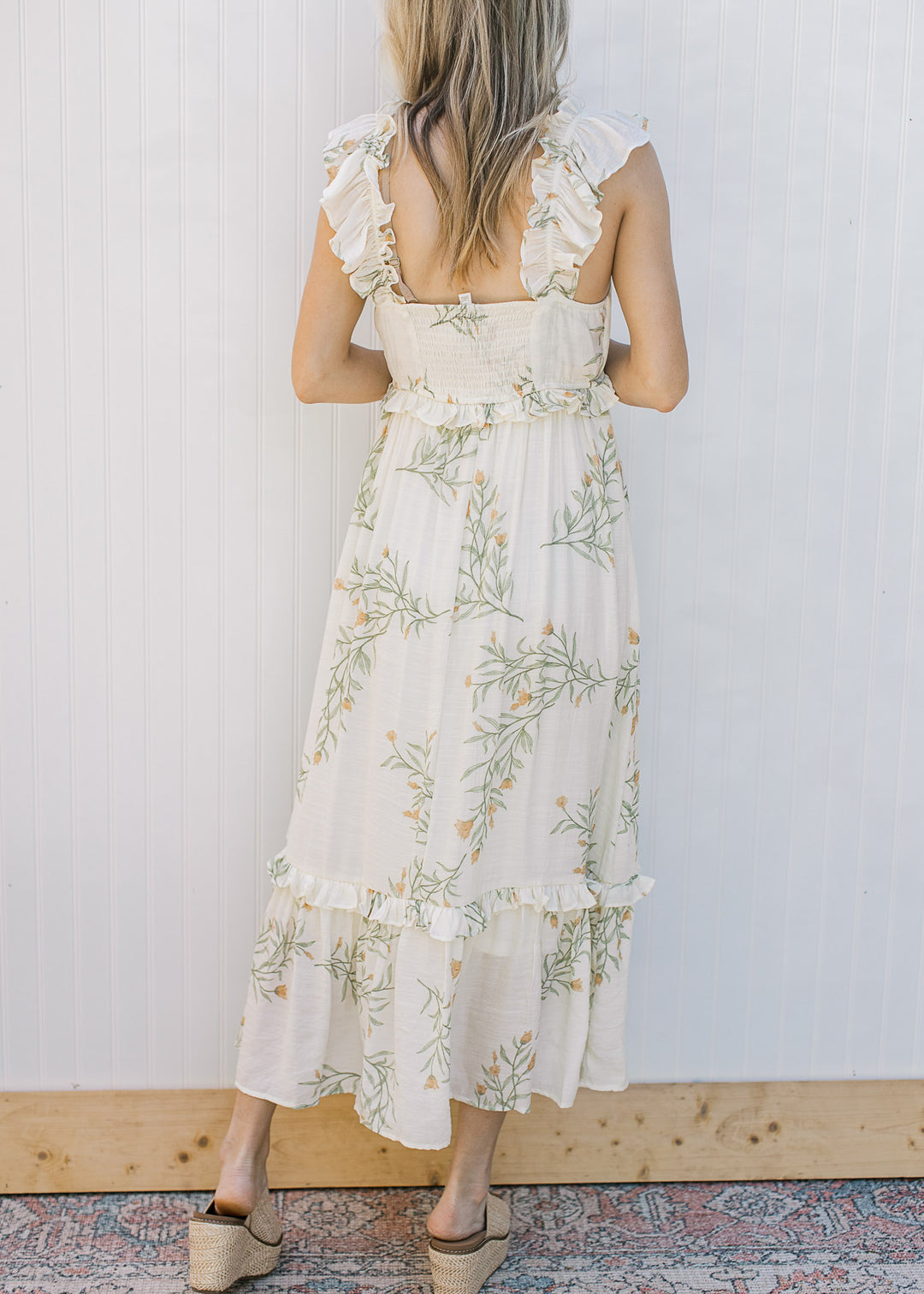 Back view of Model wearing a sleeveless, cream midi with floral, smocked back and tired ruffles.