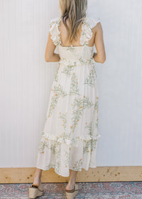 Back view of Model wearing a sleeveless, cream midi with floral, smocked back and tired ruffles.