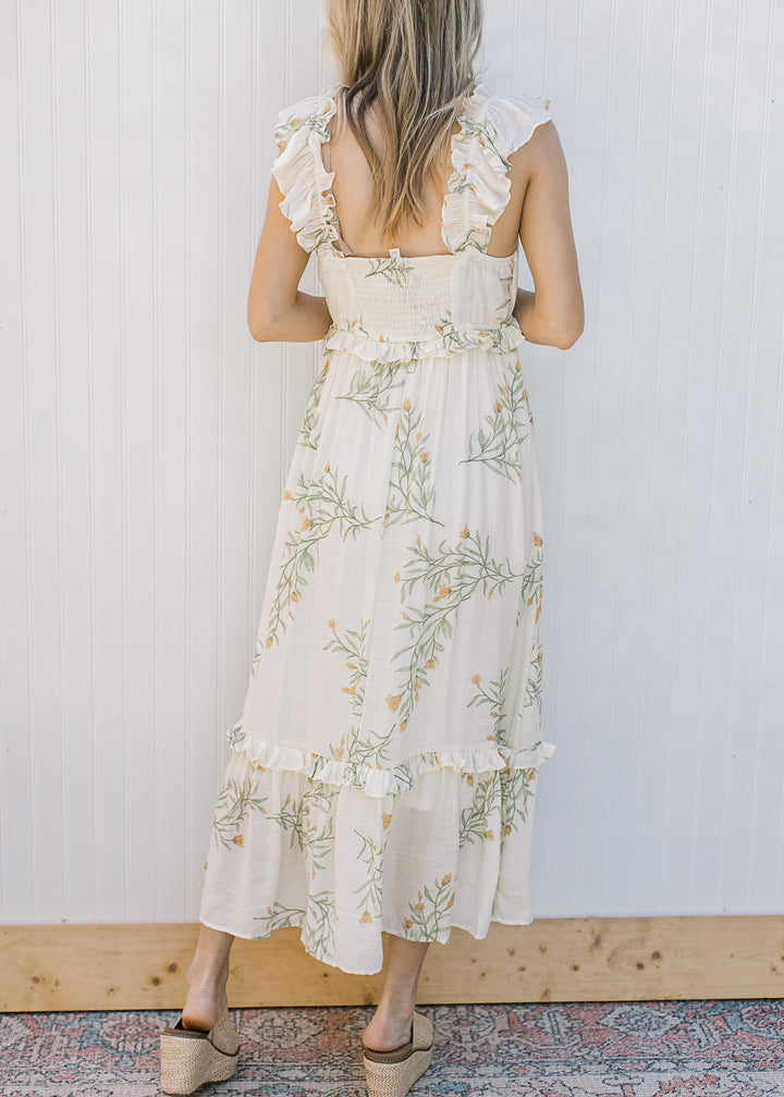 Back view of Model wearing a sleeveless, cream midi with floral, smocked back and tired ruffles.