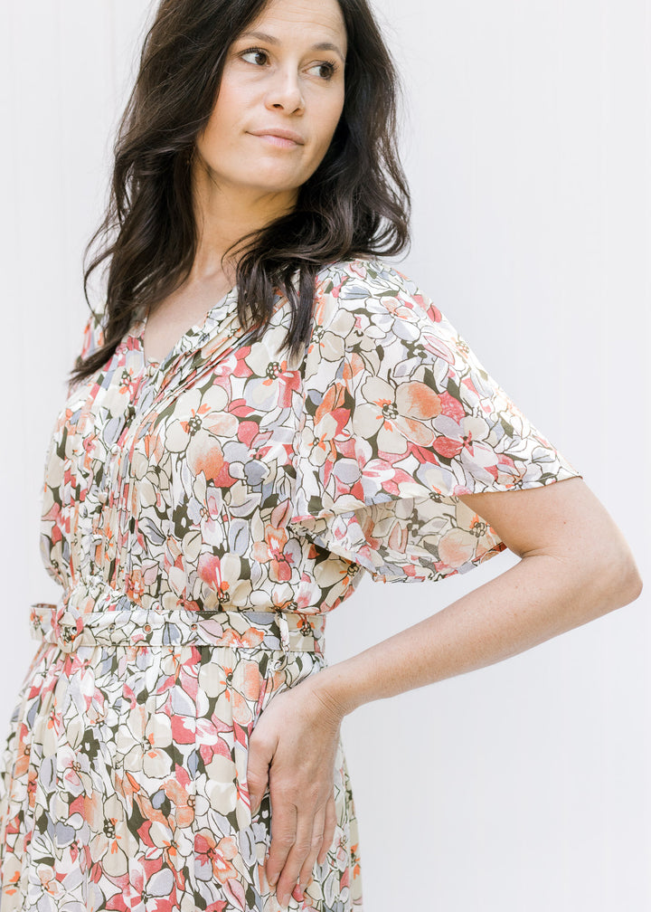 Close up view of flutter sleeve and elastic waistband with a belt on a neutral floral dress. 