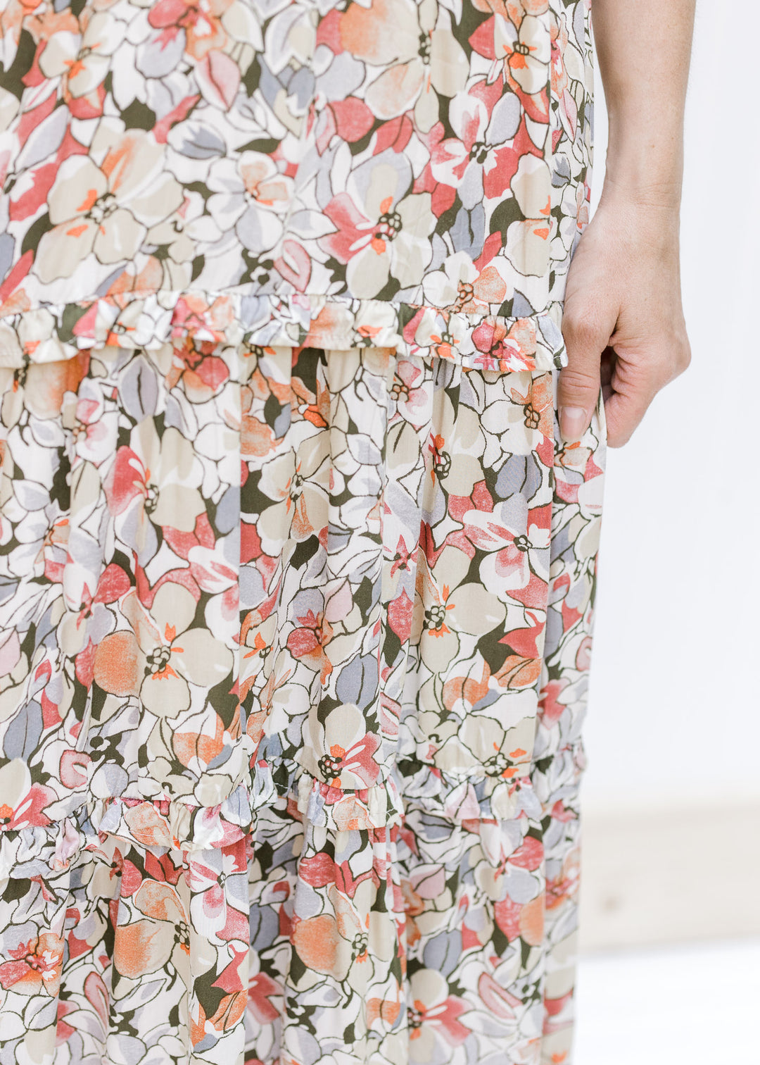 Close up view of ruffle details on the tiers of a neutral color midi dress made of rayon. 