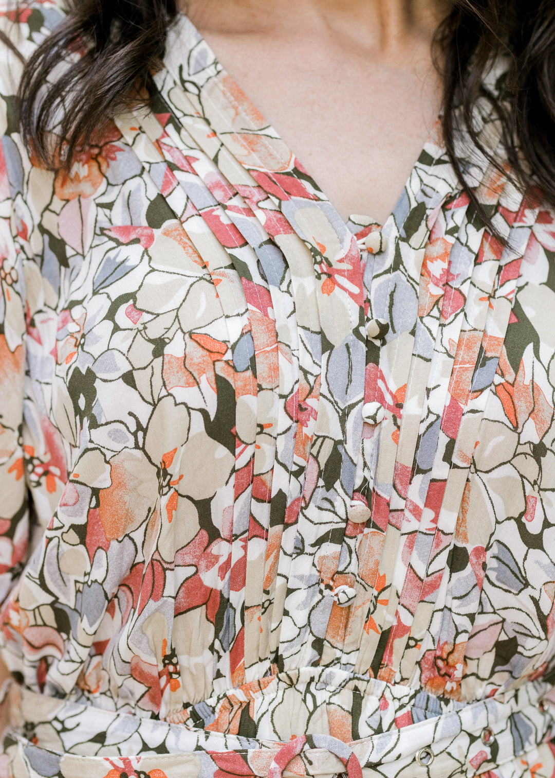 Close up of pleating on a v-neck dress with buttons and a neutral floral pattern. 