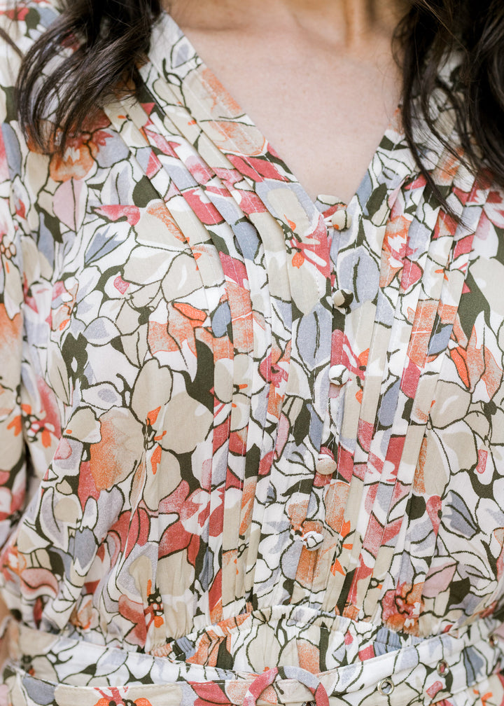 Close up of pleating on a v-neck dress with buttons and a neutral floral pattern. 