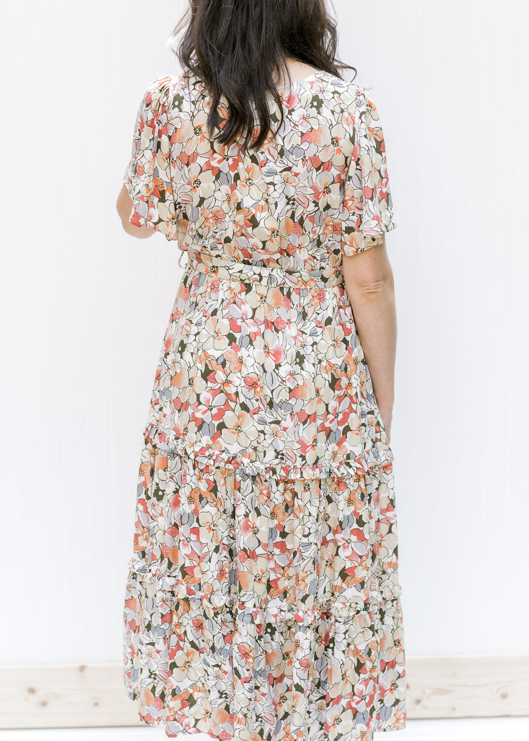 Back view of Model wearing a midi v-neck dress with a neutral floral pattern, flutter short sleeves.