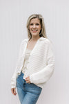 Model wearing a cream knit cardigan with a button front and long sleeves.