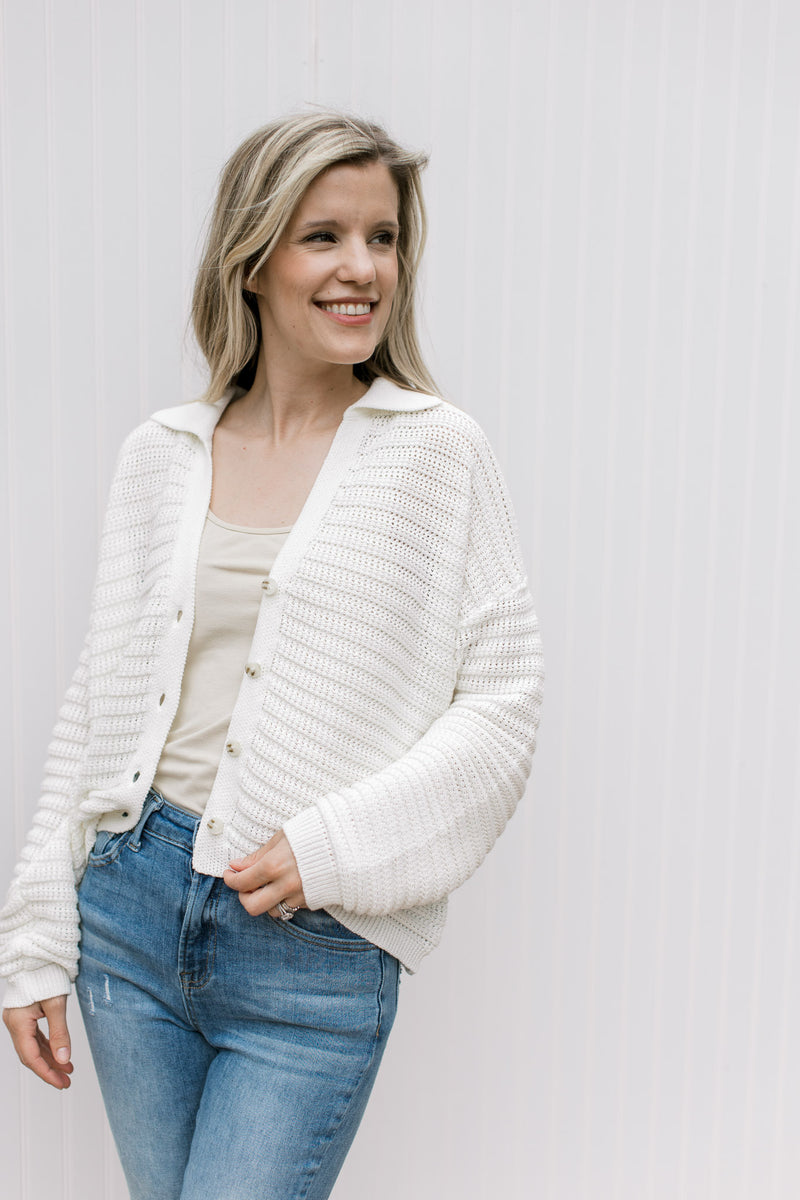 Model wearing jeans with a cream knit cardigan with a button front and long sleeves.