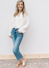 Model wearing jeans and slides with a cream knit cardigan with a button front and long sleeves.