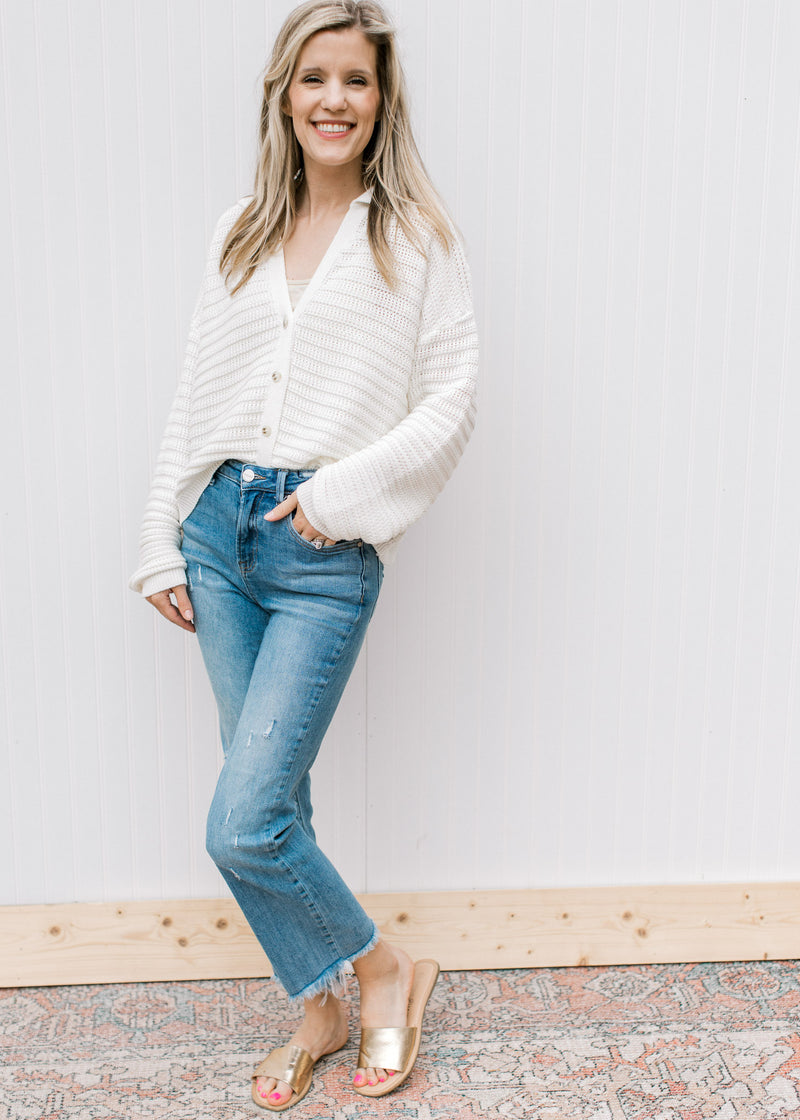 Model wearing jeans and slides with a cream knit cardigan with a button front and long sleeves.