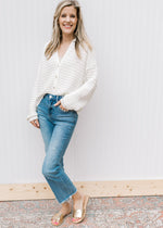 Model wearing jeans and slides with a cream knit cardigan with a button front and long sleeves.