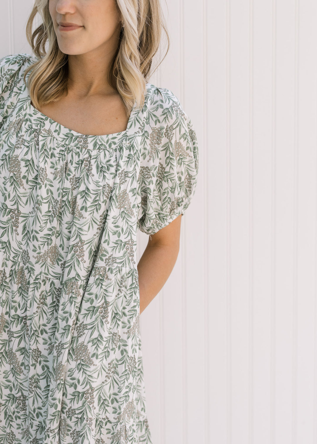 Model wearing a cream above the knees dress with a green floral pattern and a square neckline. 