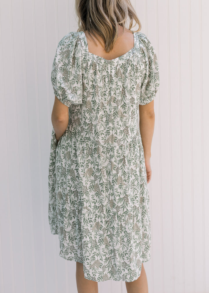 Back view of Model wearing a cream dress with a green floral pattern and a square neckline. 