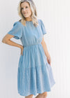 Model wearing a blue and white gingham tiered dress with an elastic waistband and short sleeves. 