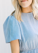 Close up view of short sleeves on a blue and white gingham tiered dress and an elastic waistband. 