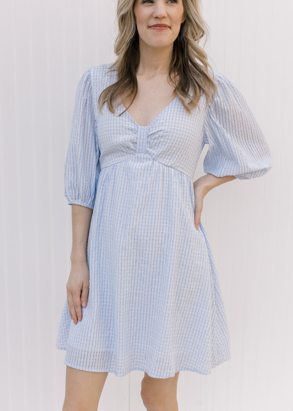 Model wearing a tone on tone checkered v-neck above the knee dress with an elbow length sleeve. 